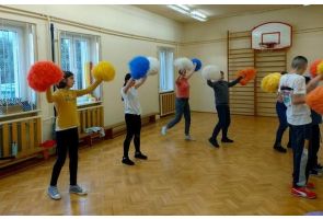 Uczniowie ćwiczą z kolorowymi pomponami podczas zajęć ruchowych.